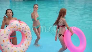 最好的朋友穿着泳衣，带着蓝色的水在游泳池里跳舞，夏天，快乐的女孩带着粉红色的充气戒指
